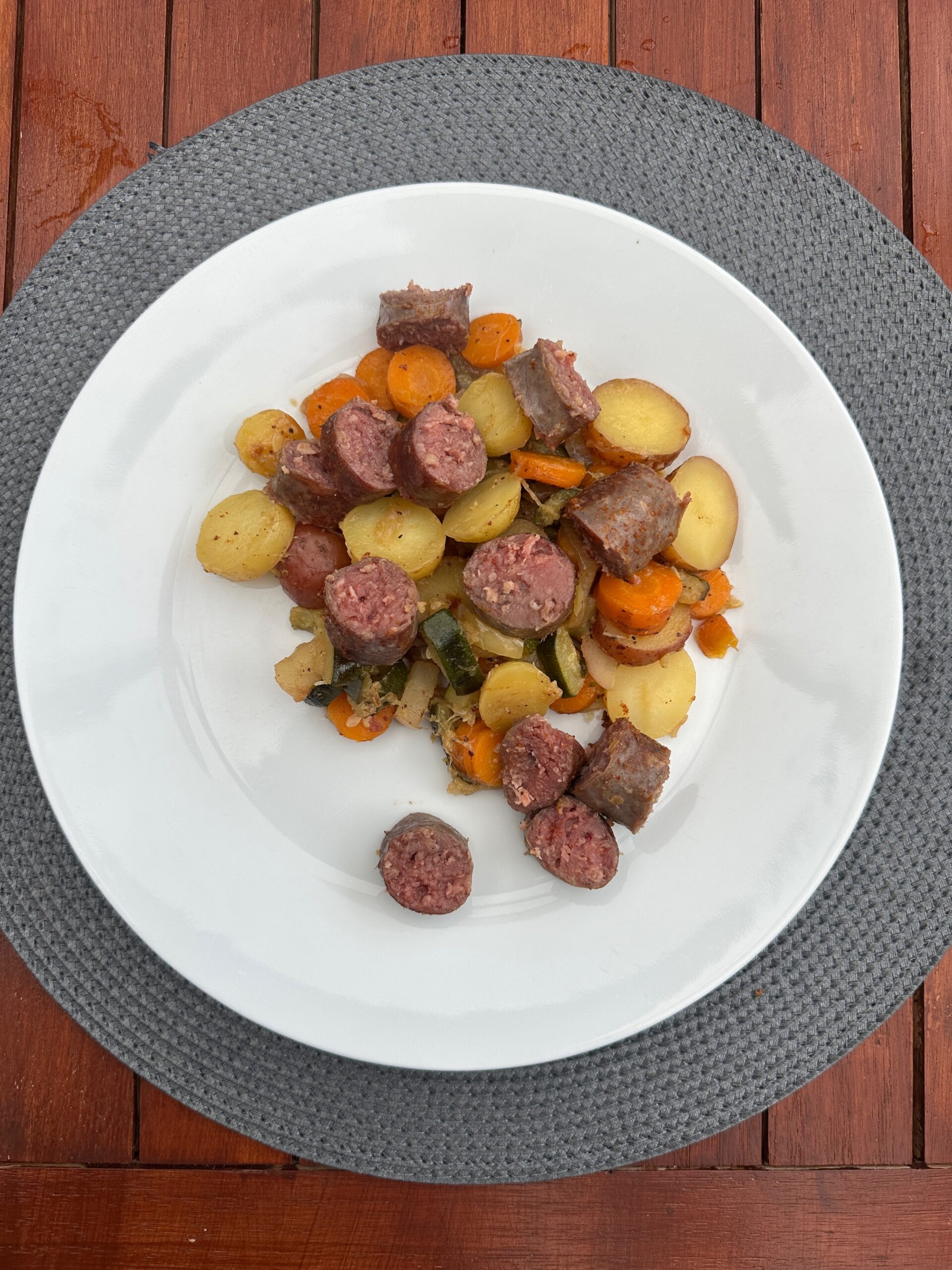 Sappige braadworst met geroosterde groenten in gietijzeren pan op kamado barbecue
