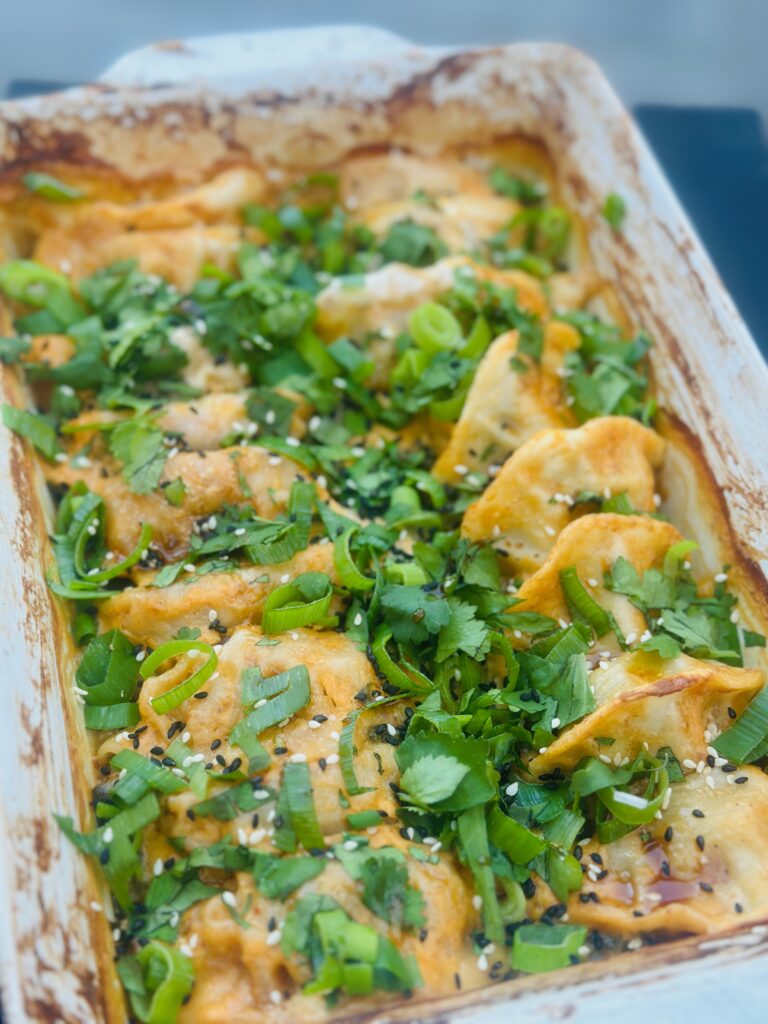 Aziatische dumpling schotel met gyoza en paksoi in vuurvaste schaal op kamado BBQ, gegarneerd met lente-ui en sesamzaadjes