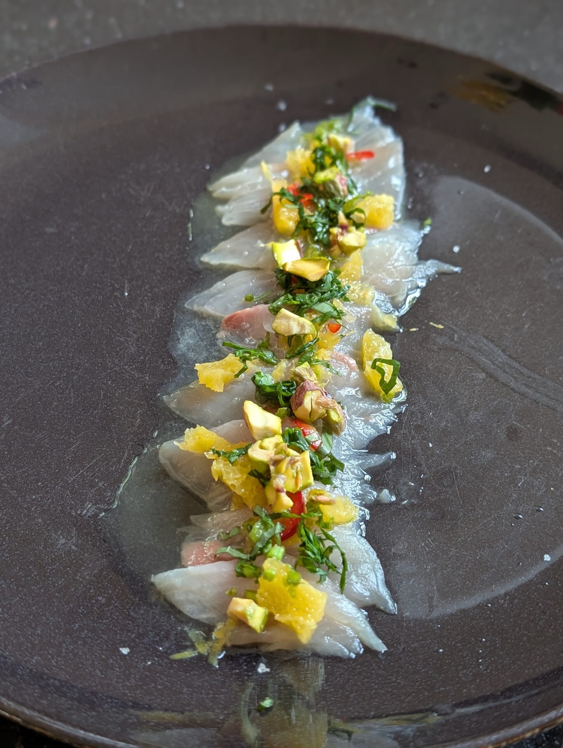 Verse zeebaars crudo gerecht op wit bord met citrus en kruiden - BBQ Broers recept